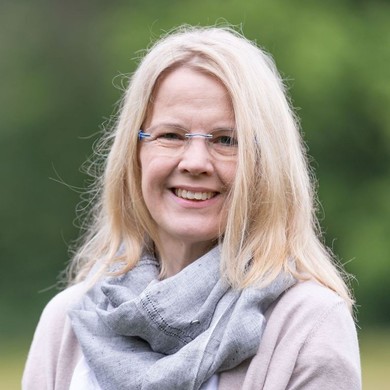 Portrait einer Frau mit blonden, schulterlangen Haaren und einem Tuch um den Hals vor grünem Hintergrund