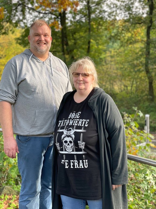 Eine blonde Frau mit Brille und ein größerer Mann mit kurzen Haaren stehen nebeneinander (vergrößerte Bildansicht wird geöffnet)