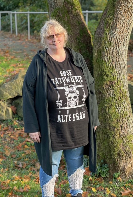 Eine blonde Frau mit Brille steht vor einem Baum (vergrößerte Bildansicht wird geöffnet)