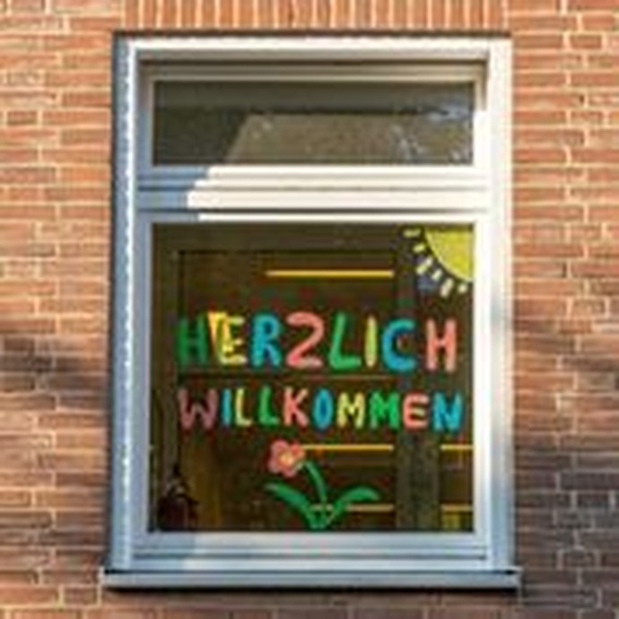 Ein Fenster ist mit bunter Farbe mit dem Schriftzug "Herzlich Willkommen" bemalt (vergrößerte Bildansicht wird geöffnet)