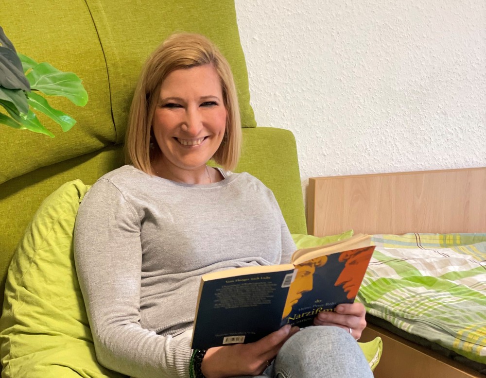 Frau mit schulterlangen Haaren sitzt in einem grünen Sitzsack und liest ein Buch