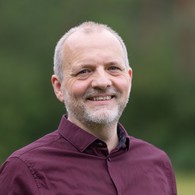 Portraitfoto Mann mit bordauxrotem Hemd, kurzem Bart und kurzen Haaren