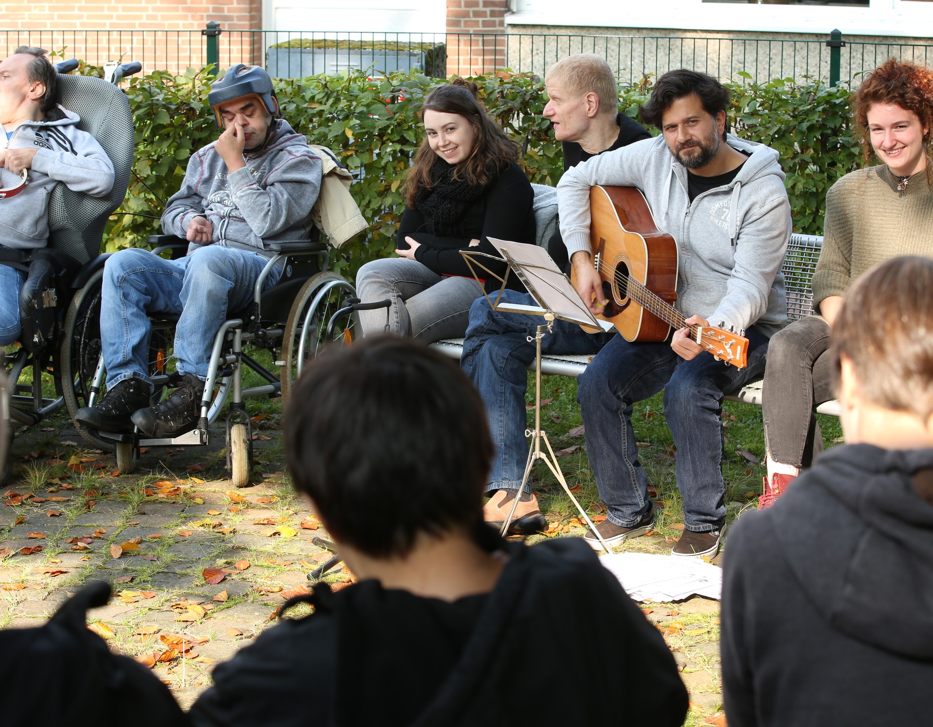 Viele Menschen sitzen zusammen in einem Kreis und musizieren, ein Mann spielt auf einer Gitarre