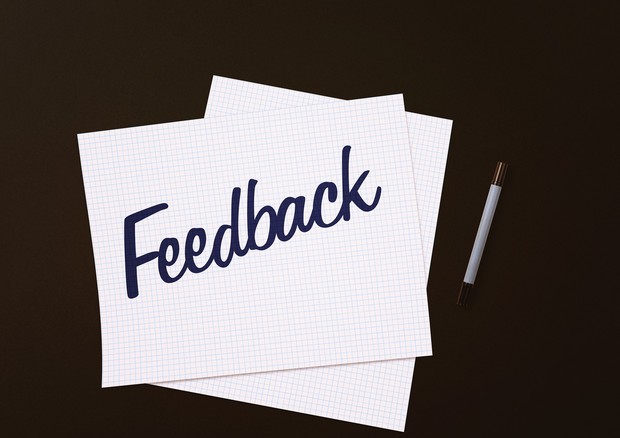Zwei weiße Blätter liegen übereinander, ein Stift liegt daneben und der Schriftzug Feedback ist lesbar. Der Hintergrund ist schwarz eingefärbt