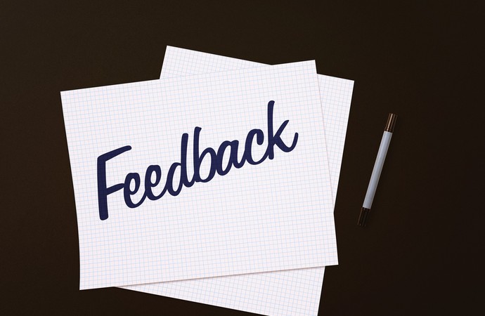 Zwei weiße, karrierte Blätter liegen übereinander auf schwarzem Hintergrund, auf ihnen der Schriftzug Feedback in blau