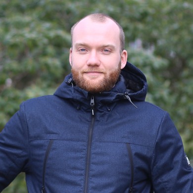 Portrait eines Mannes mit sehr kurzen Haaren, Bart und dunkelblauer Jacke vor grünem Hintergrund