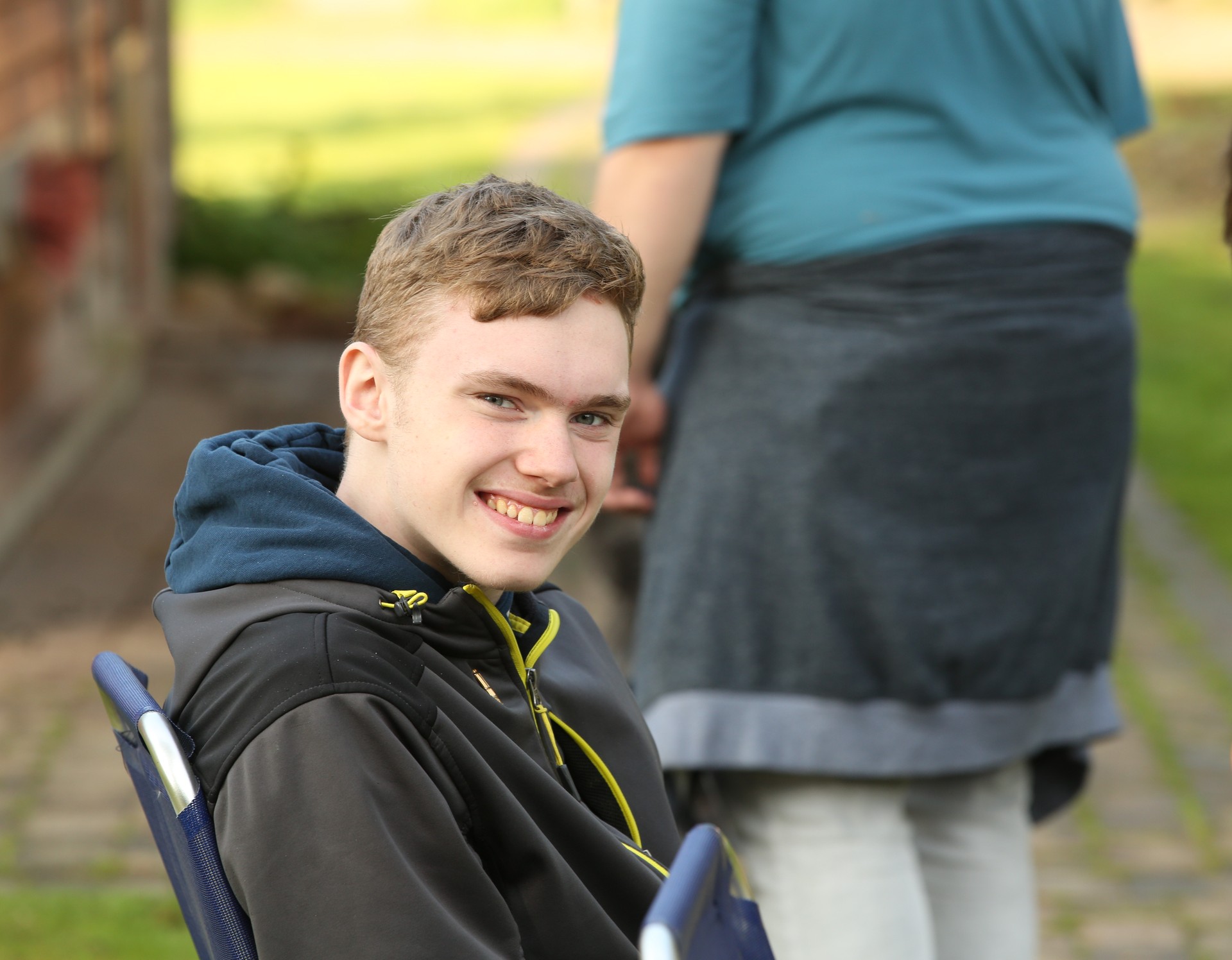 Ein Junge mit blionden Haaren sitzt auf einem Kettcar und lacht in die Kamera
