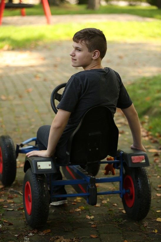 Ein Junge sitzt auf einem roten Kettcar und schaut über seine linke Schulter.