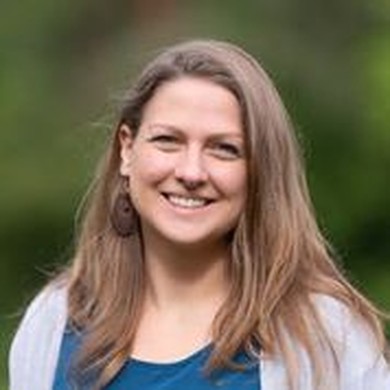 Frau mit langen, braunen Haaren vor grünem Hintergrund. Die Frau lächelt.